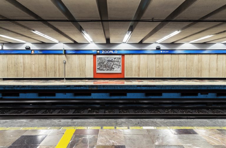 Fotografia de la estacion Zocalo de la linea 2, se logra ver las vías y publicidad en la pared
            